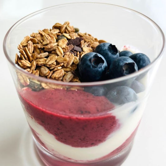 Glas met yoghurt, rode vruchtencoulis, granola en verse blauwe bessen